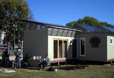 Photo showing the exterior of a solar home, with the porch and landscaping removed and team members taking a break in the front yard.