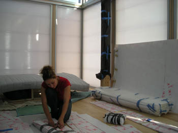 Photo of a woman taping bundles of items together in a house with translucent, white, softly glowing walls.
