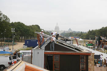 Photo of three men on the roof of a house, wearing safety gear and installing solar panels. The Capitol building is in the background.