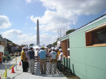 Photo of a number of people carrying a metal grid, with the house from the University of Colorado at Boulder on the right and the Washington Monument in the background.
