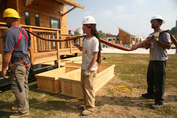 Photo of three men standing in profile, holding a water house; the University of Illinois solar house is seen in the background.