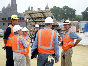 Photo of three men and two women wearing day-glo orange vests and hard hats standing in a circle on the National Mall.