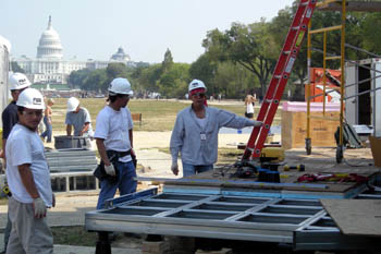 A photo of a partially built sun deck on the exterior of a solar house, with three team members at work. The U.S. Capitol building is visible in the background.