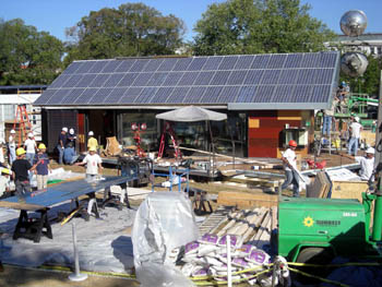 Aerial photo showing the exterior a of solar house under construction, with every spot of the yard covered with materials and equipment.
