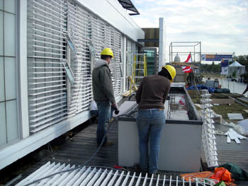 Photo of three people with hardhats working on the ramp and railing leading to the front door of a solar house.