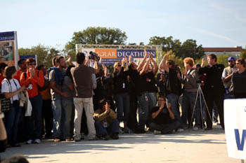 Photo of a crowd of about 40 people, with about 10 of them applauding with their hands held high. A large banner with the Solar Decathlon name and logo is in the background. 