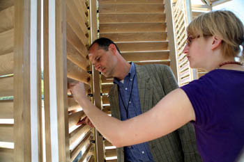 Photo of a man in a business suit inspecting louvered shutters, while a woman in a blue T-shirt looks on. 