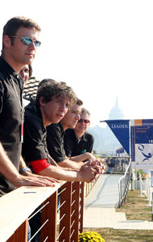Photo of four people in black polo shirts standing in line leaning on the railing of a deck. The U.S. Capitol Building is visible in the background.