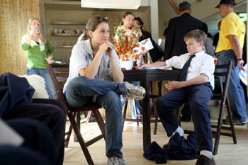 Photo of a college-age woman and a young boy sitting at a table, with several people in the background.