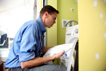 Photo of a man in a blue shirt putting a towel into a washing machine.