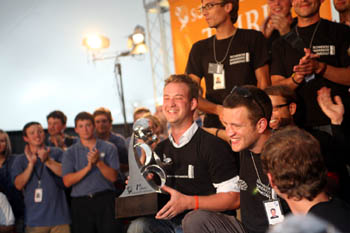 Photo of six team members grouped together, with one smiling man holding a silver trophy.