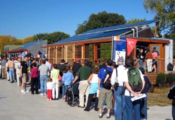 Aerial photograph of a long line of people forming a line in front of a solar house.