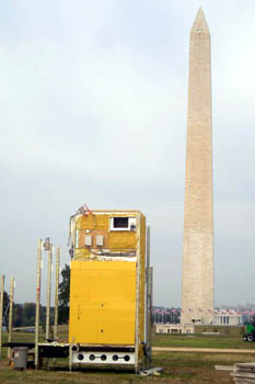 Photo of a rectangular structure with sparse metal framework; the Washington Monument is in the background.