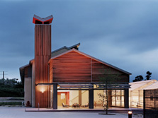 Photo of a wooden, home-like building that is used for lab and office space. The building has a tall chimney on one side and large glass panels that open like garage doors.