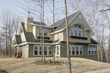 Photo of a traditional-looking two-story home, set among trees, with solar panels on the roof.