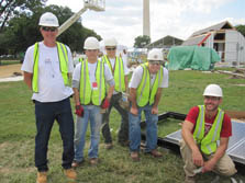 Photo of a group of five men wearing construction gear. They are posing next to solar electric panels on their assigned lot for the Solar Decathlon.