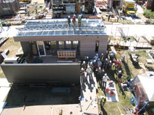 Aerial photo of a house under construction with people in hard hats standing on a ramp leading up to the house and on the roof and waving at the camera.
