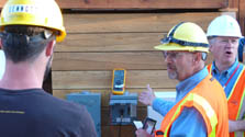 Photo of a man checking a voltage meter that measures power. Two other men are looking on.