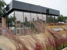 Photo of a glass house with PV panels lining the upper section. Tall grasses jut from the landscaping in front.