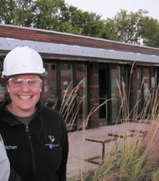 Photo of a young woman in a white hard hat. She is standing in front of the Penn State house and smiling.