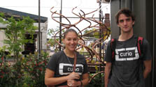 Photo of a young woman and young man in front of a hanging set of copper tubes and garden area.