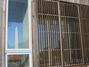 Photo of a window that is reflecting the image of the Washington Monument. To the right of the window are wooden slats.