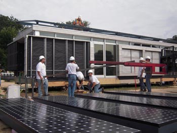 Photo of six men wearing hardhats and standing around an extended hoist. Behind them is the Kentucky team house. In the foreground is a series of solar electric panels sitting side by side.