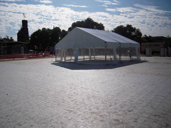 Photo of a white event tent with clear sides standing on white plastic flooring. The Smithsonian Castle, against a blue sky with white clouds, shows in the background.