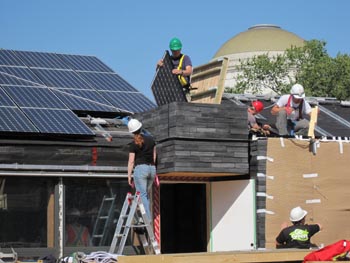 Photo of people wearing hard hats and working on the roof of a house to install a photovoltaic panel.