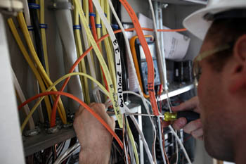 Photo of a person using a screwdriver while working in an electrical box filled with multicolored wires.