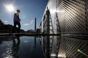 Photo of a silhouette of man walking on a deck near a pool of water. The deck is connected to a building with  walls of perforated metal.