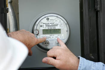 Photo of an electric meter and two hand pointing to the reading.