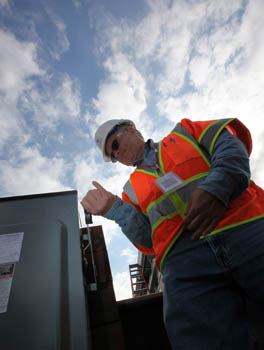 Photo of a man wearing a hard hat and safety vest flipping the switch on an electrical box.
