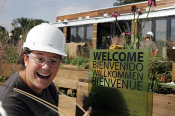 Photo of a woman wearing a hard hat and smiling next to a sign. The sign says "Welcome" in four languages.