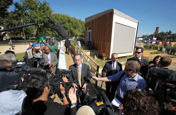 Photo of Steven Chu standing at the end of a ramp leading to the Team California house. Surrounding him are numerous media representatives holding microphones and cameras.