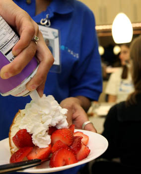 Photo of a hand adding canned whipped cream to a plate of strawberry shortcake.