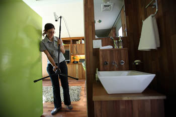 Photo of a  young woman carrying a sensor mounted to a tripod through a hallway area. To the right in the foreground, the basin of the washroom is visible.