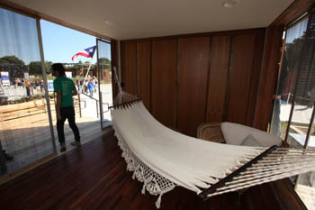 Photo of a hammock hanging in a wood-paneled and floored room with sliding doors. A person is exiting the left door.