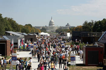 Photo of a crowd of visitors on Decathlete Way in the solar village. The team houses line the sides of the walkway, and the U.S. Capitol is visible in the background.