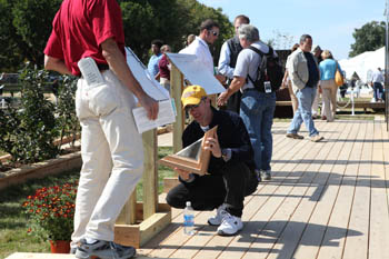 Photo of a man crouched on an exterior deck and inspecting a triangular section of wood-framed glass.