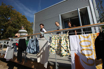 Photo of a line of laundry on the back deck of the Rice University house. On the deck, several people exit a door of the house.