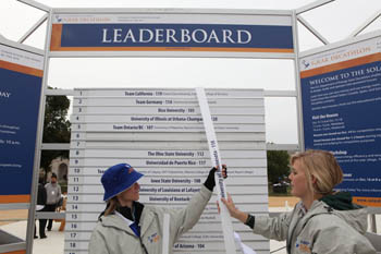 Photo of two woman standing in front of a leaderboard and moving the slat labeled University of Minnesota.