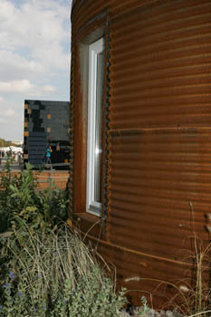 Photo of the edge of a curved rusted structure in the foreground and a cubic, dark, and reflective structure in the background.
