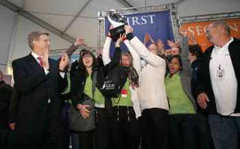 Photo of Team Germany students cheering and hoisting their first-place trophy over the heads. Daneil Poneman claps and looks on.