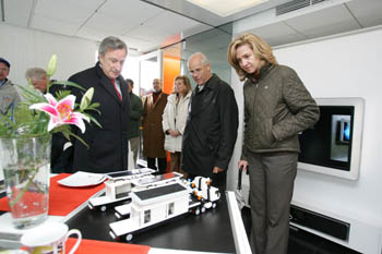 Princess Cristina and two men examine scale models of a home loaded on semi-trailers on the dining table of the Team Spain house.