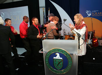 Photo of a group of students on stage clapping and celebrating. In front is a lectern with the U.S. Department of Energy seal.