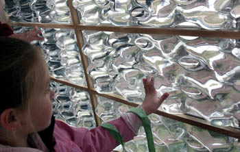 Photo of a young girl touching a glass wall with an irregular surface.
