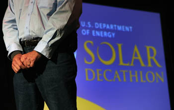 Photo of a man's hands and torso. In the background is a large screen that displays "U.S. Department of Energy Solar Decathlon."