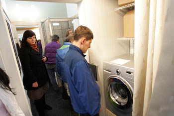 Photo of people touring the Iowa State University house. In the foreground, a man stares at single-unit washer and dryer.
