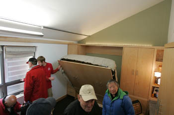 Photo of a group of visitors inside Iowa State's house. In the corner, a student folds a bed back into a wall unit.